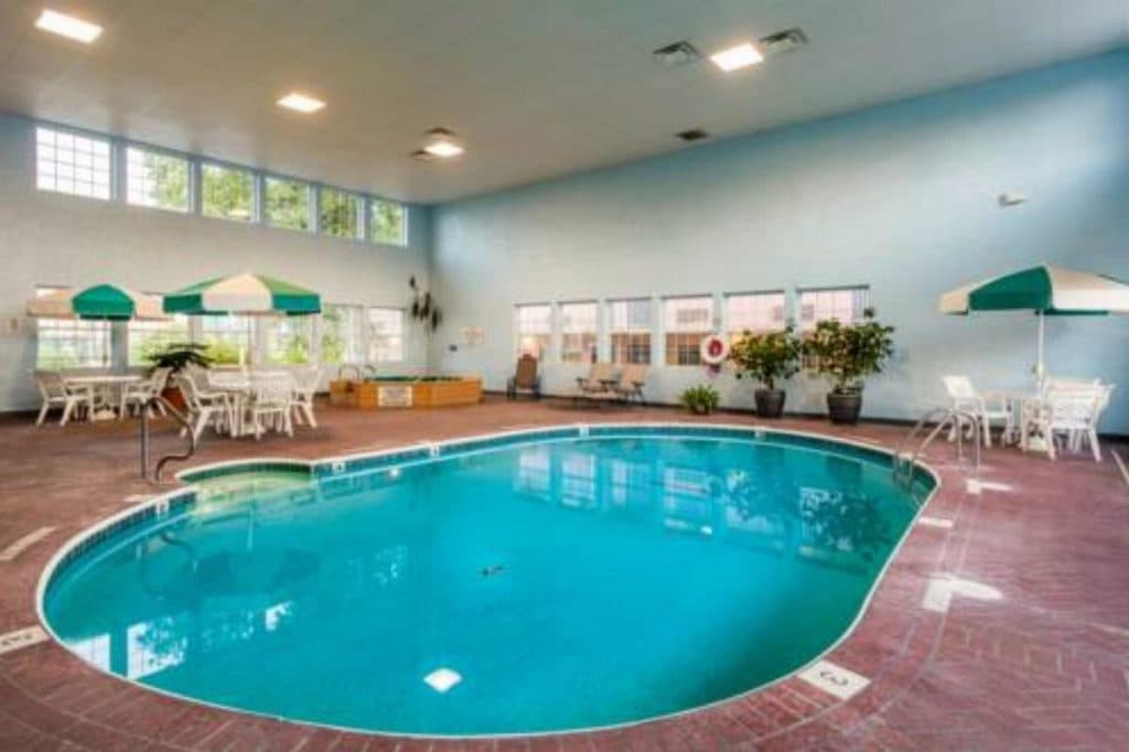 Indoor pool area at Angel Inn Central in Branson MO with a large swimming pool, poolside seating, and umbrellas