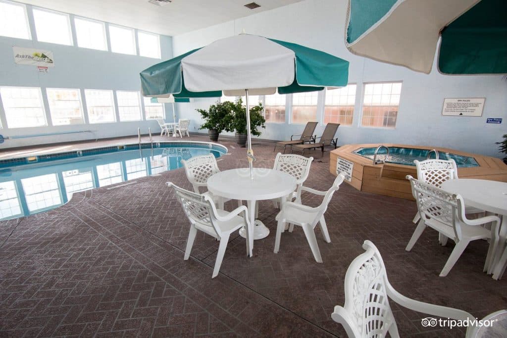 Indoor pool area at Angel Inn Central in Branson MO with a swimming pool, hot tub, tables, chairs, and umbrella seating