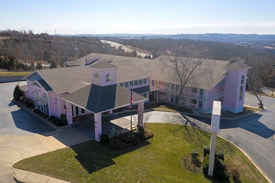 Aerial view of the Angel Inn Central hotel exterior in Branson, Missouri with a pink building, covered entrance, and landscaped grounds