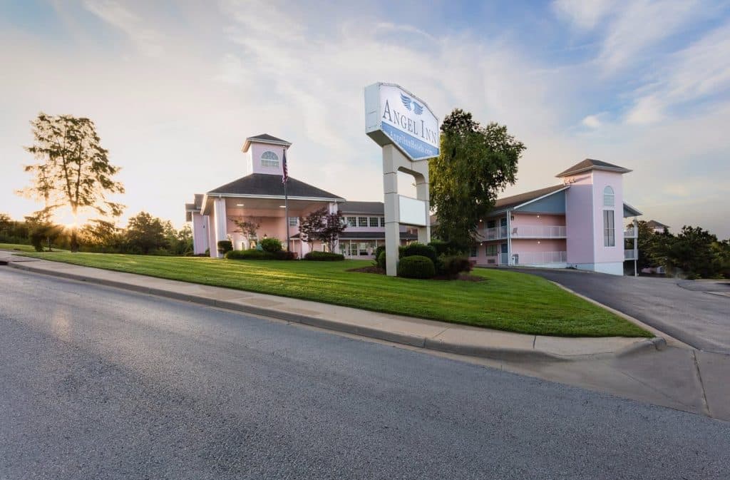 Exterior view of Angel Inn Central in Branson, Missouri, with the hotel sign, front entrance, landscaped lawn, and driveway at sunset
