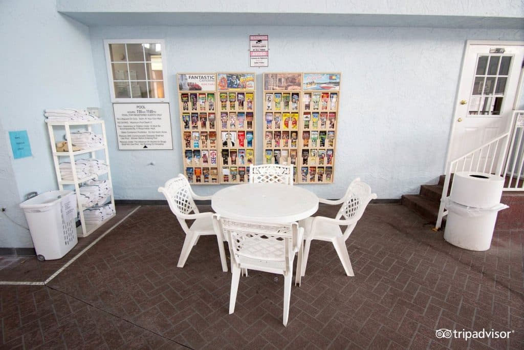 Outdoor patio seating area at Angel Inn Central in Branson MO with white chairs, a round table, towel shelf, and brochure displays