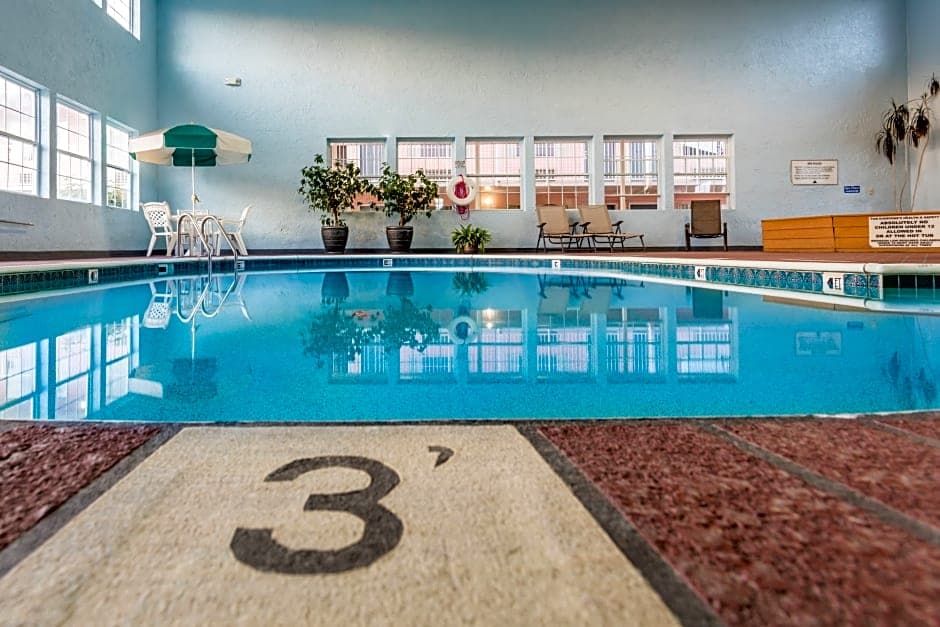 Indoor swimming pool area at Angel Inn Central in Branson, MO with a large tiled pool, lounge chairs, and windows along the wall