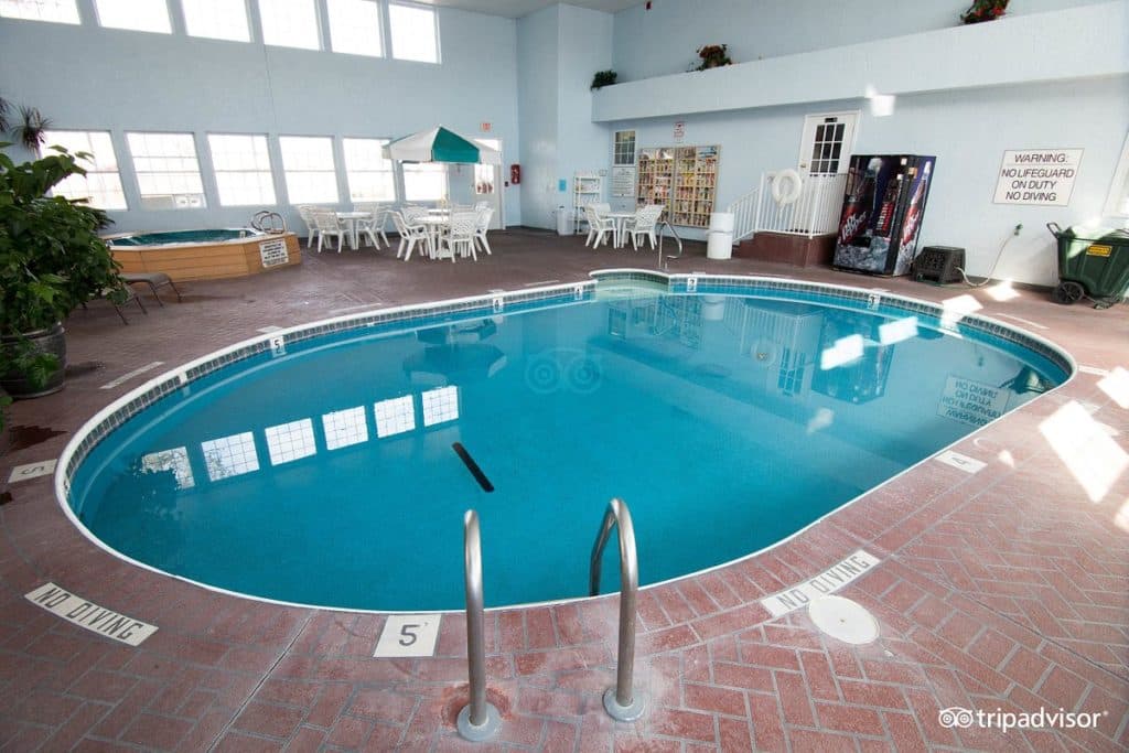 Indoor pool area at Angel Inn Central in Branson, MO with an oval swimming pool, hot tub, and lounge seating