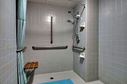 Accessible shower bathroom with tiled walls, grab bars, handheld showerhead, and shower seat at Angel Inn Central in Branson, Missouri