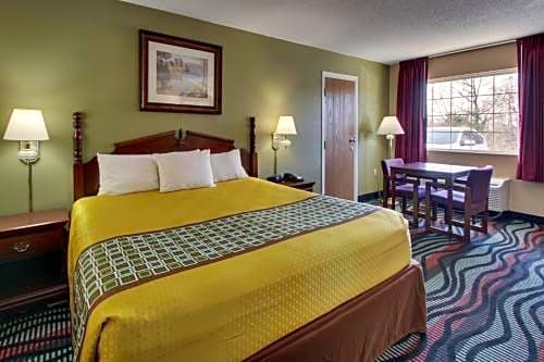 Queen guest room at Angel Inn Central in Branson MO with a queen bed, bedside lamps, window table and chairs, and patterned carpet