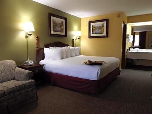Queen room at Angel Inn Central in Branson MO with a queen bed, armchair, wall sconces, framed art, and a vanity area visible through the doorway