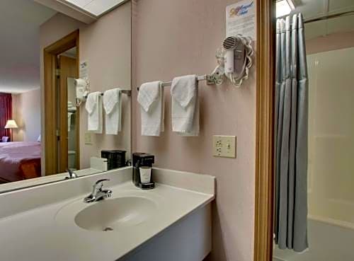Bathroom vanity area with sink, mirror, wall mounted hair dryer, towels, and a shower curtain in an Angel Inn Central Queen Room in Branson, Missouri