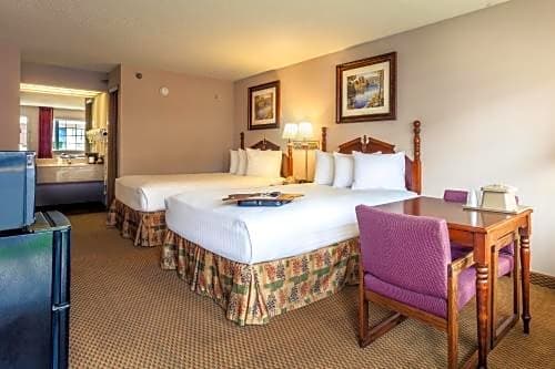 Two queen bed guest room at Angel Inn Central in Branson MO with a small table, TV, and vanity area visible